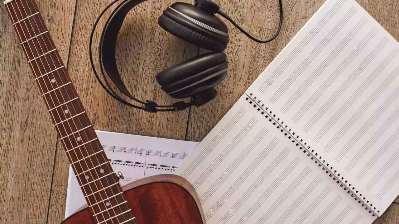 Guitarra con partituras, auriculares y cuaderno de música sobre un suelo de madera en una escuela de música en Madrid