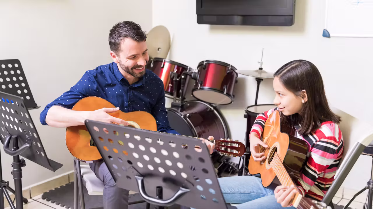 Profesor enseñando guitarra a niños, adolescentes y adultos durante una clase en Madrid